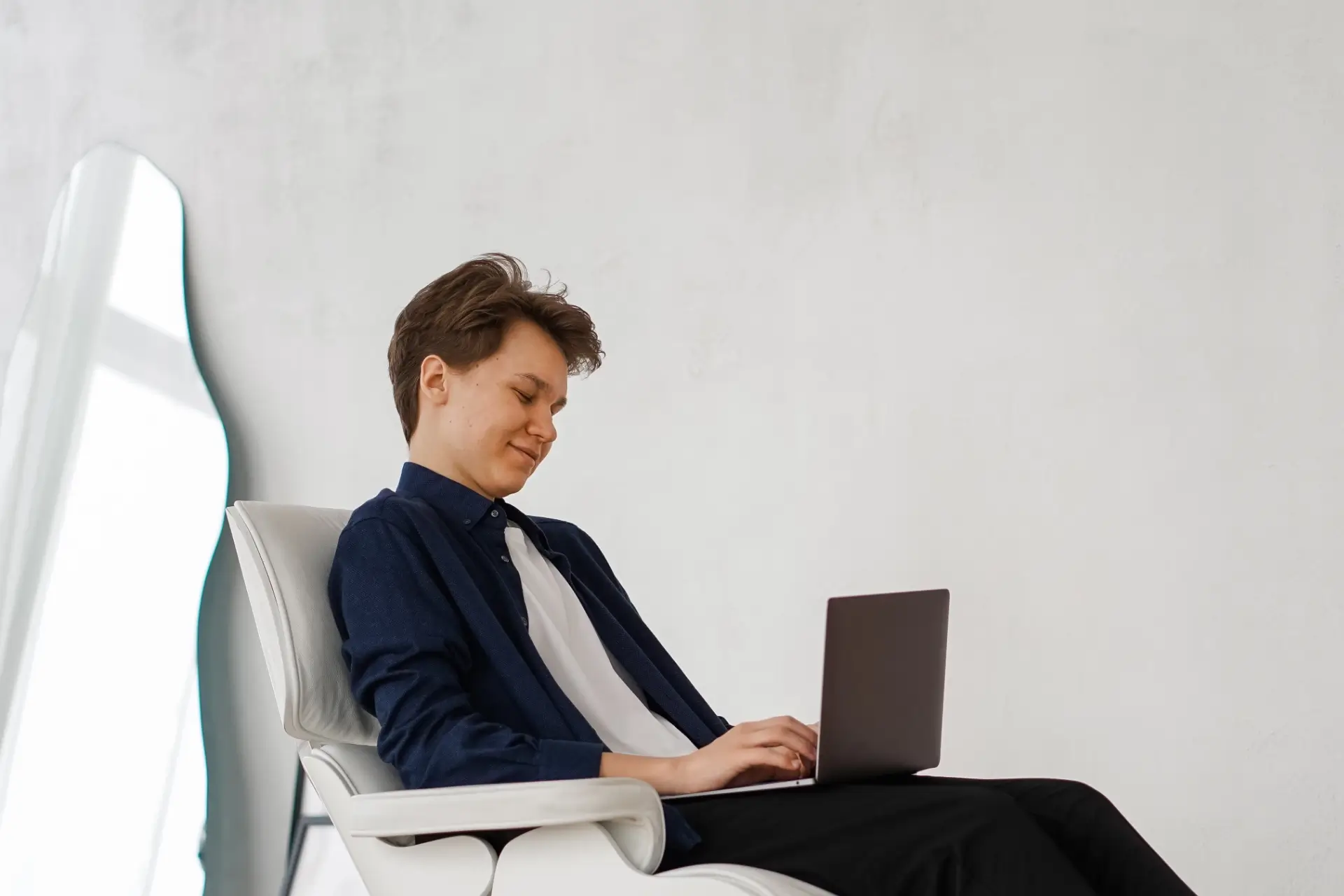 Fiatal férfi egy széken ül a laptopon dolgozik.